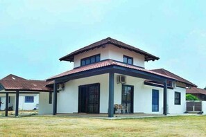 Uma casa de dois andares com telhado plano, varanda coberta e quintal cercado.