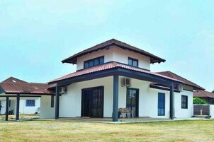 Una casa de dos pisos con techo plano, un porche cubierto y patio cercado.