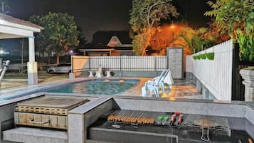 An outdoor pool area with a barbecue grill, lounge chairs, and a covered seating area.