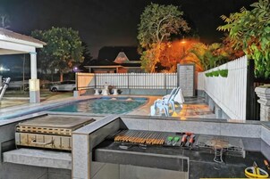 An outdoor pool area with a barbecue grill, lounge chairs, and a covered seating area.