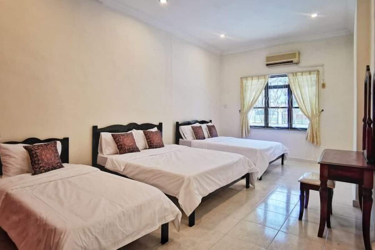 A hotel room with three single beds, a wooden nightstand, and a window with curtains.