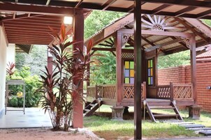 A covered outdoor area with a wooden structure, steps leading to a door, and a small garden with plants.