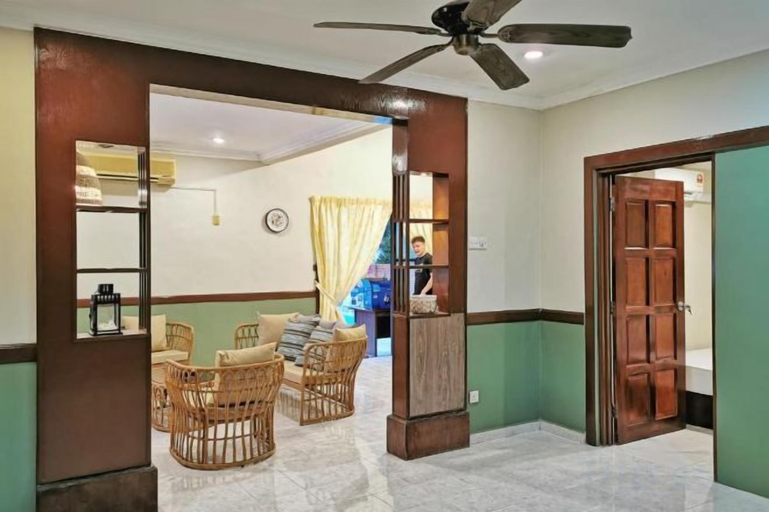 A hotel lobby with a reception desk, seating area with wicker chairs, and a ceiling fan.