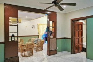 Un vestíbulo de hotel con mostrador de recepción, zona de estar con sillas de mimbre y un ventilador de techo.