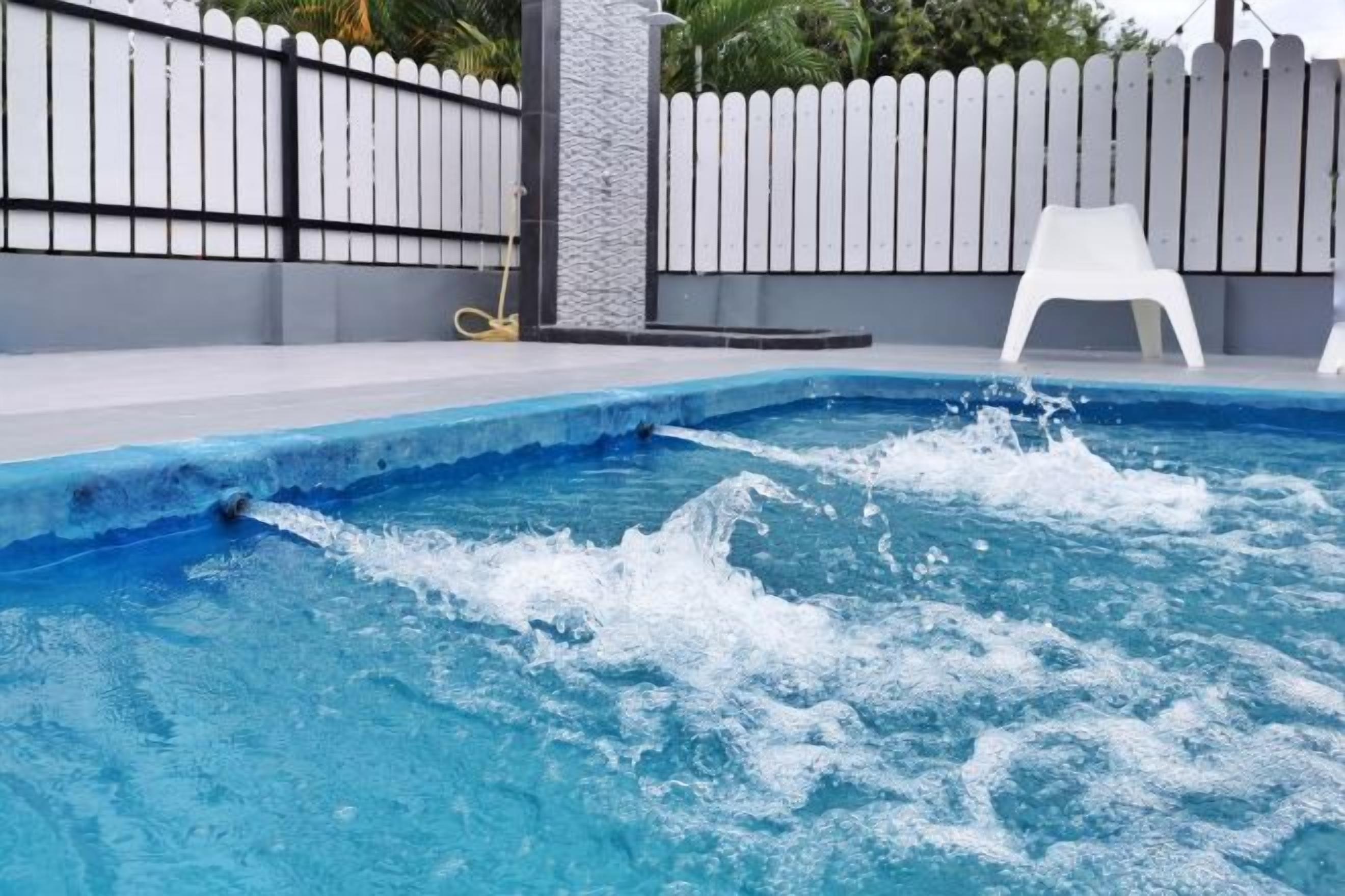 A swimming pool with water splashing, a white fence, and a white plastic chair.