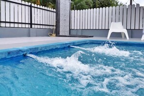 Una piscina con agua salpicando, una valla blanca y una silla de plástico blanca.