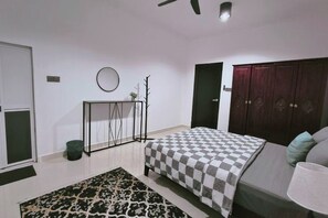A bedroom with a checkered bedspread, a bedside table with a lamp, a wardrobe, and a patterned rug. - Sky312 Muslim Homestay (Langkawi)
