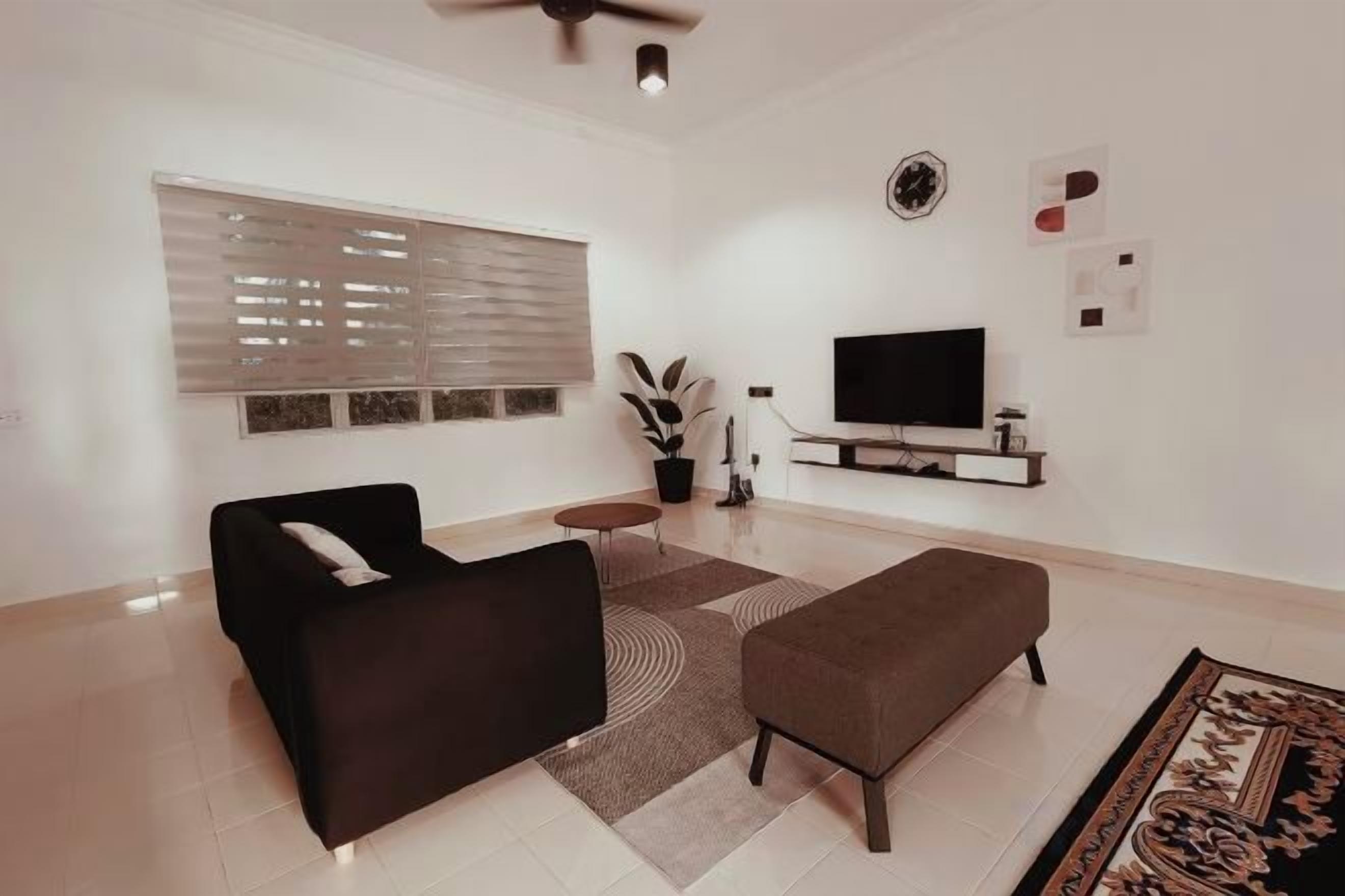 A modern living room with a sofa, ottoman, and a flat-screen TV on a stand.
