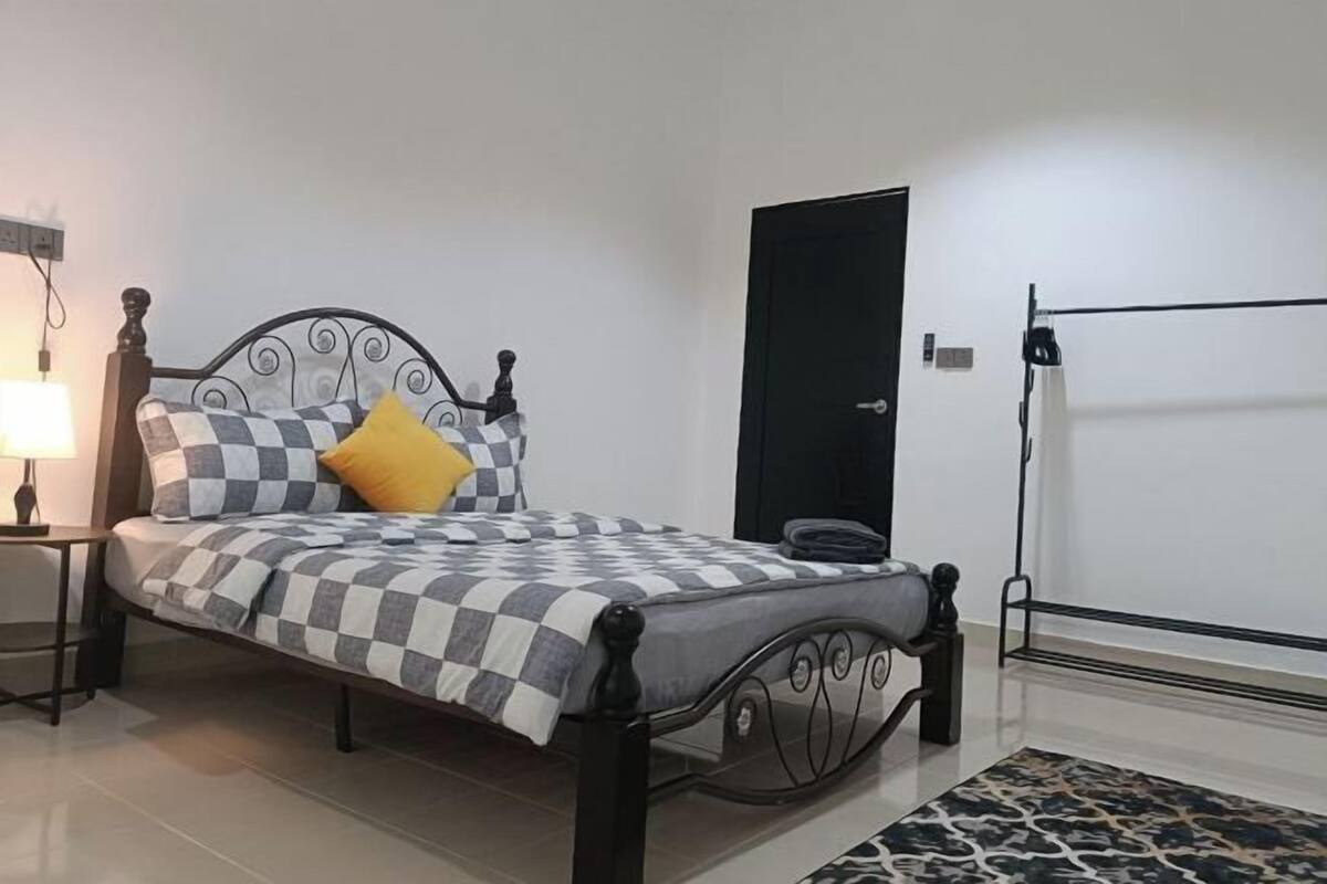 A neatly made bed with a checkered bedspread and a single yellow pillow.