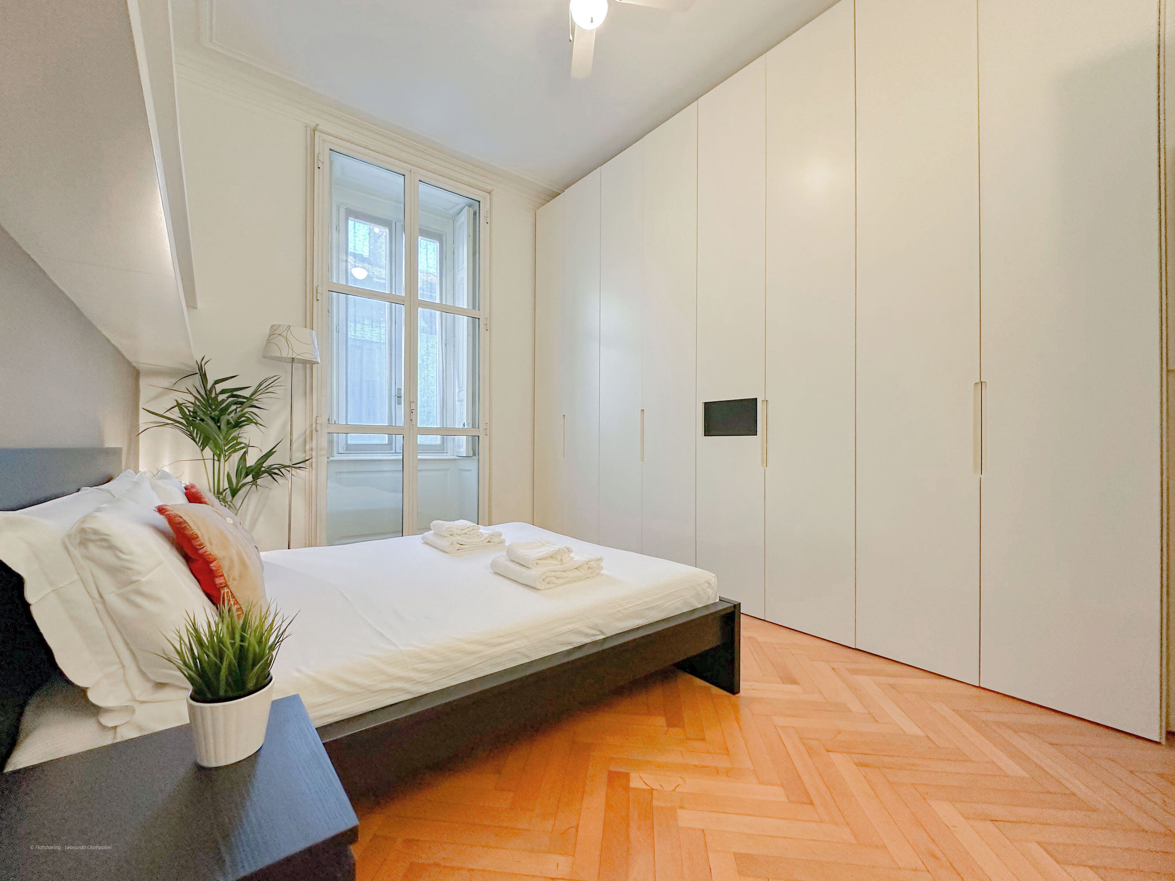 A bedroom with a bed, a potted plant, a window, and a wardrobe.