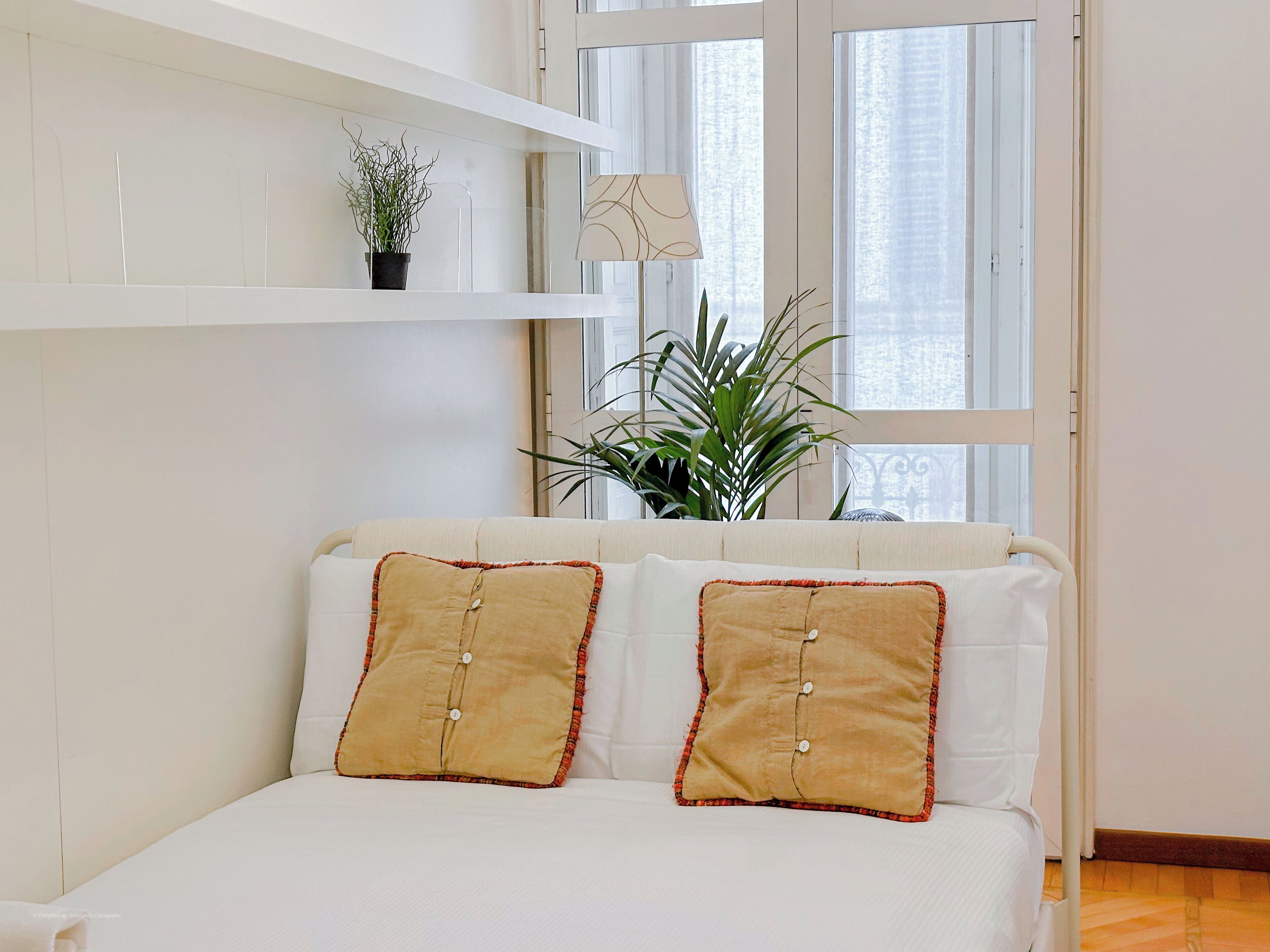 A bedroom with a bed, two pillows, a potted plant, a lamp, and a window.