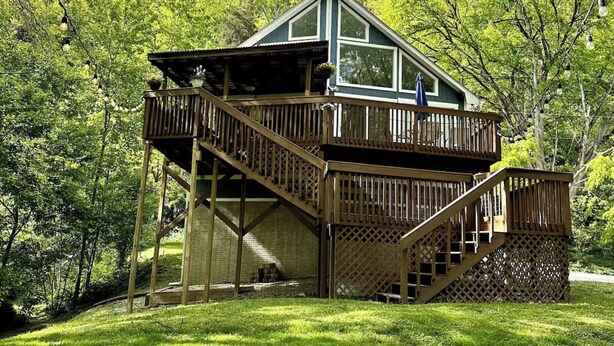 A two-story wooden cabin with a balcony, surrounded by trees. - River Relaxation - Calm Riverfront Home in Winchester Kentucky (Winchester)