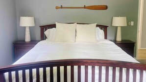 A bed with white bedding, two bedside lamps, and two wooden paddles mounted on the wall. - River Relaxation - Calm Riverfront Home in Winchester Kentucky (Winchester)
