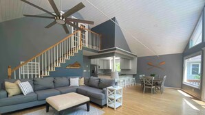 A spacious living area with a grey sectional sofa, a wooden floor, a ceiling fan, and a staircase leading to an upper level. - River Relaxation - Calm Riverfront Home in Winchester Kentucky (Winchester)