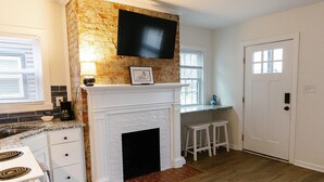 A kitchen with a brick accent wall, a white fireplace, a TV mounted above it, and a door with a window. - Big Blue - Stylish Studio in Downtown Lexington (Lexington)