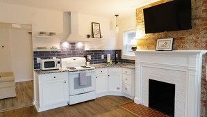 A compact kitchen with white cabinetry, a built-in microwave, a stove, and a brick accent wall. - Big Blue - Stylish Studio in Downtown Lexington (Lexington)
