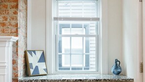 A kitchen with a white countertop, a window with blinds, two white stools, and a blue vase on the counter. - Big Blue - Stylish Studio in Downtown Lexington (Lexington)