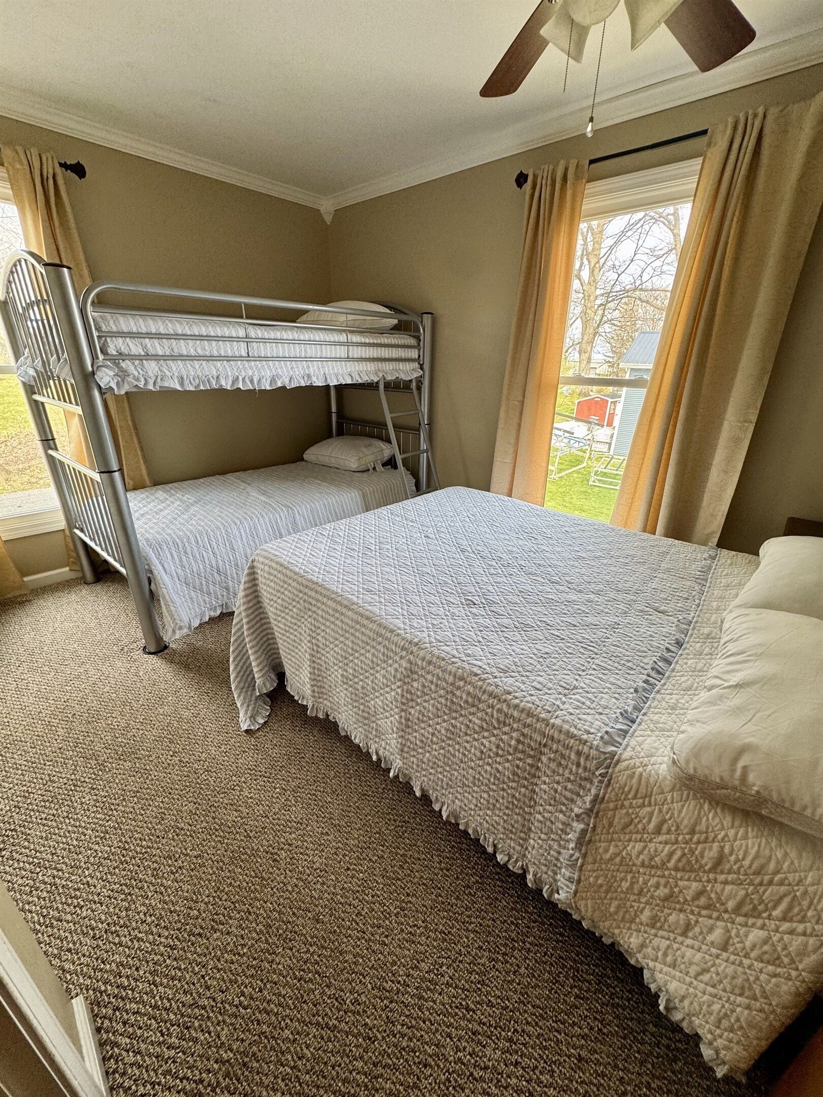 Habitación con literas, ventilador de techo, ventana grande con cortinas y piso alfombrado.