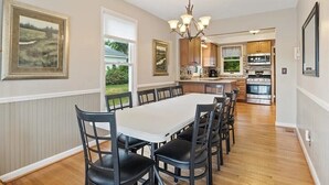 A dining area with a white table and black chairs, a chandelier, and framed artwork on the walls. - Sodus Bay View at the Point (Sodus Point)