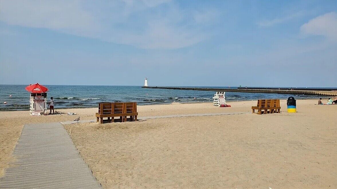 Une plage dotée d’un poste de surveillance pour les sauveteurs, de bancs en bois et d’une jetée qui s’avance dans l’eau.