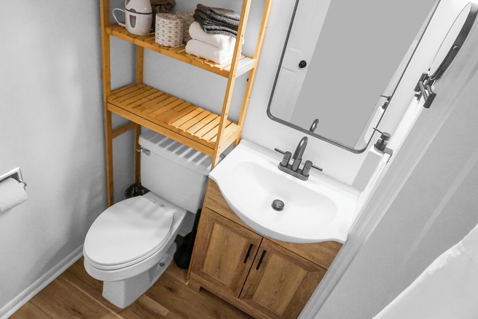 Une petite salle de bain comprenant des toilettes, un lavabo et une étagère en bois située au-dessus des toilettes.