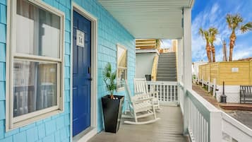 A blue house with a porch, a black planter, white rocking chairs, and a wooden staircase leading to a deck.