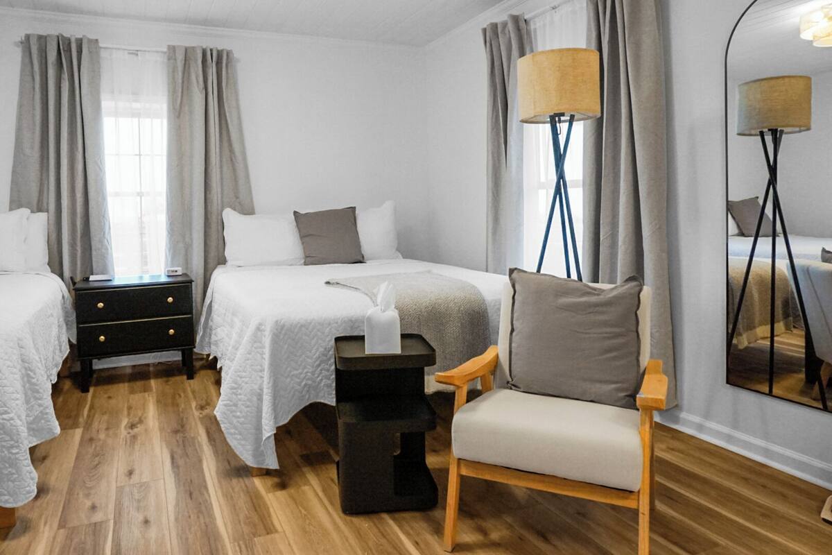 A hotel room with two beds, a wooden floor, a chair, a nightstand, and a lamp.