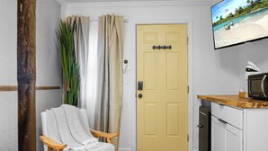 A room with a wooden chair, a yellow door, a television, and a kitchen area with a microwave. - Boardwalk Inn (Carolina Beach)