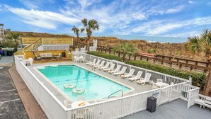 A rectangular pool with lounge chairs and a deck area, surrounded by a white fence and palm trees. - Boardwalk Inn (Carolina Beach)