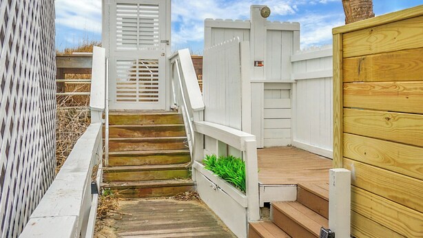 A wooden staircase leading to a white door with a window, surrounded by a white fence and a wooden deck. - Boardwalk Inn (Carolina Beach)