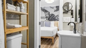 A bedroom with a bed, a wooden shelf with towels, a white sink, and a mirror. - Boardwalk Inn (Carolina Beach)