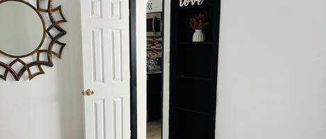 A room with a bed, a white door, a black door, a mirror, and a shelf with a 'love' sign.