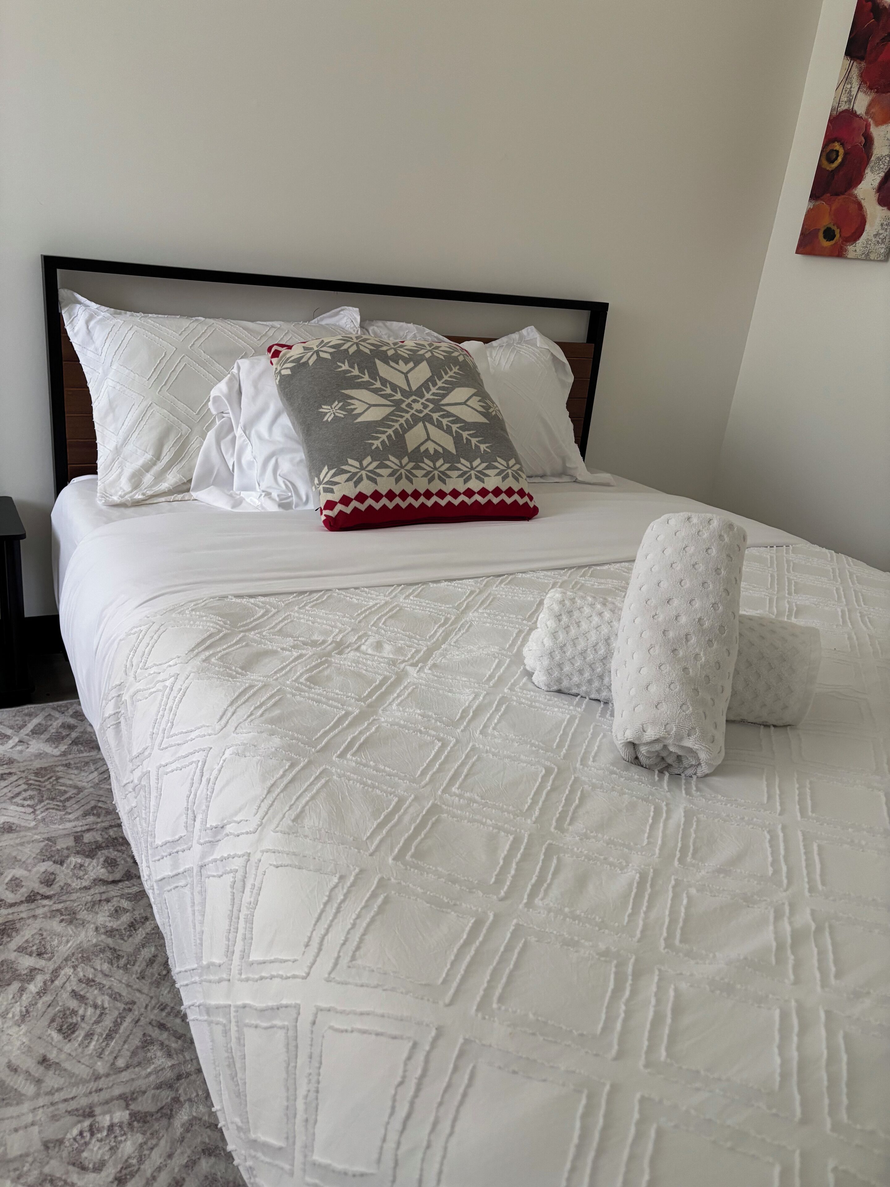 Un lit bien fait, avec une couvre-lit à motifs, des oreillers et une serviette enroulée.