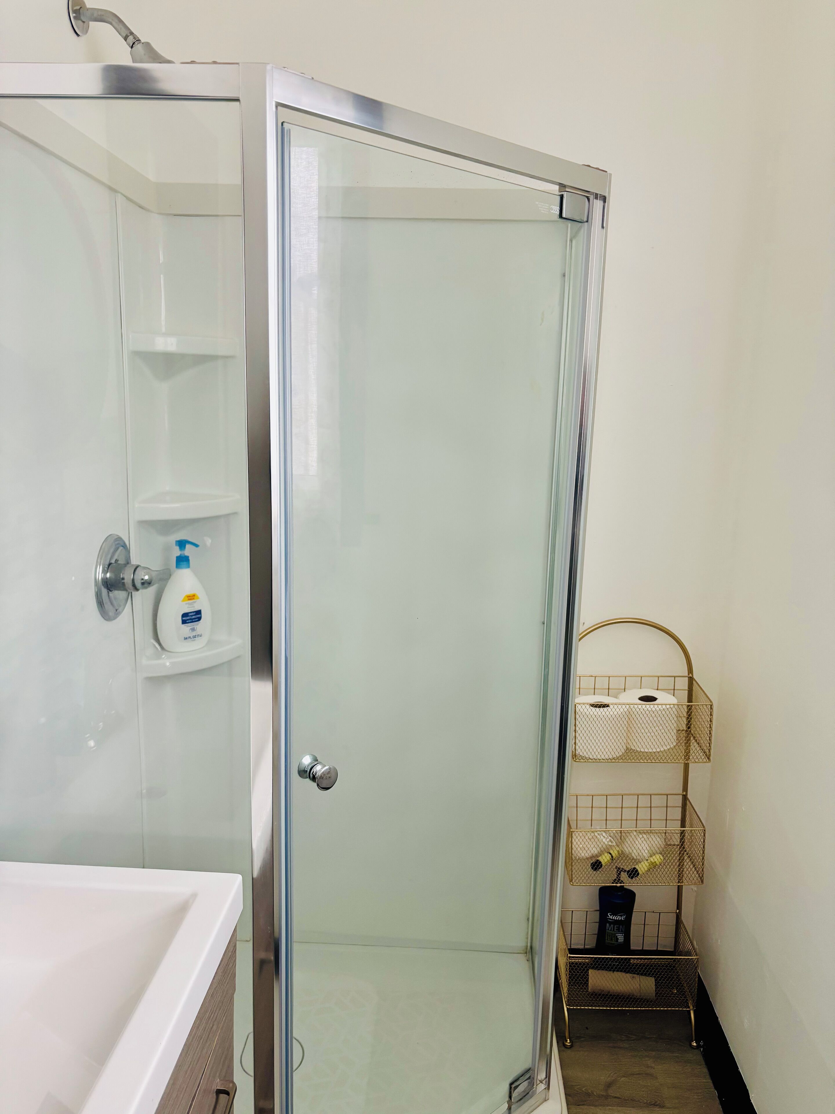 Une salle de bain avec une douche à parois de verre, un lavabo blanc et une étagère contenant des articles de toilette.