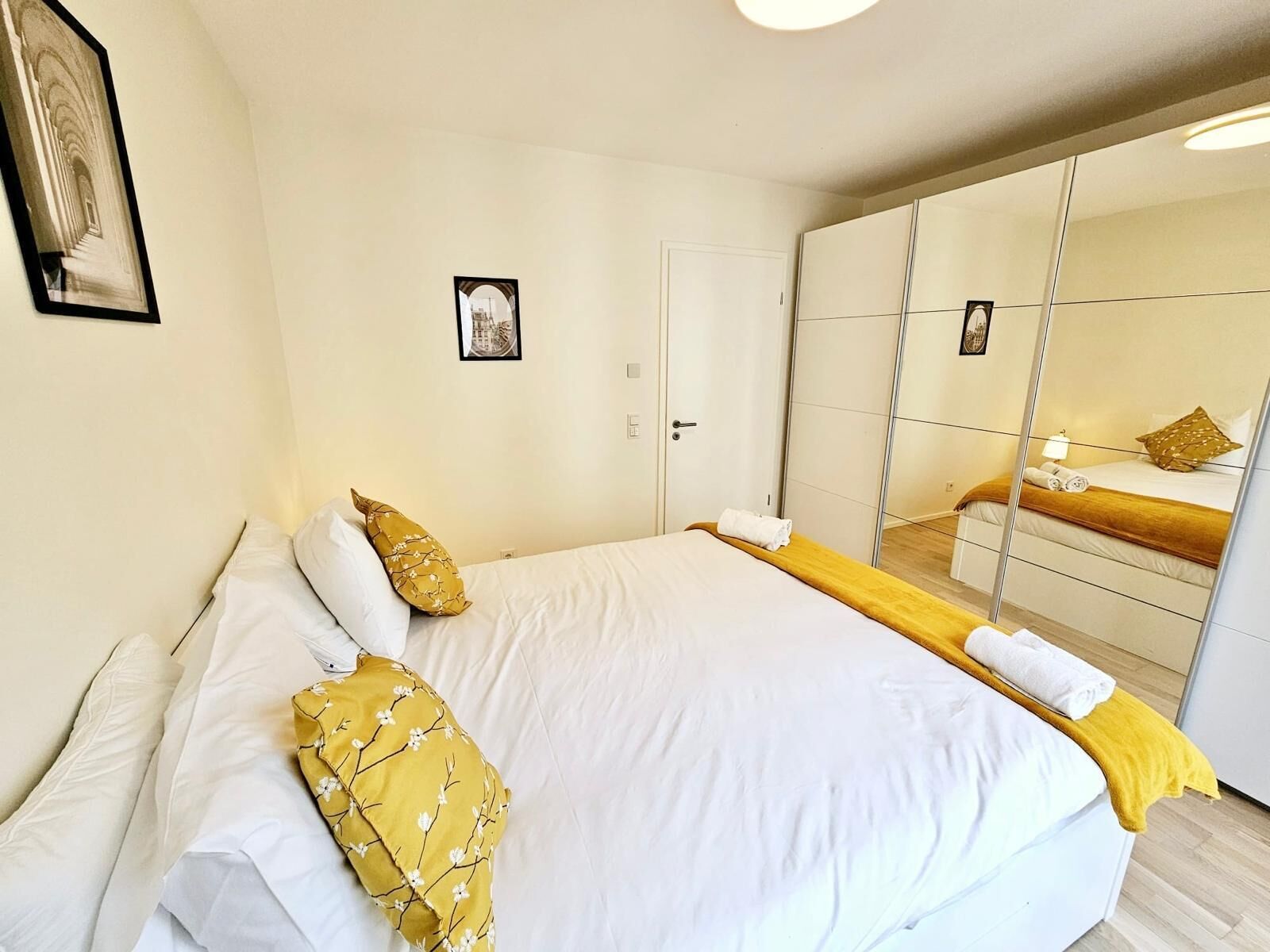 Hotellihuone, jossa on suuri sänky, vaatekaappi, peili ja seinällä oleva kehystetty taulu.
