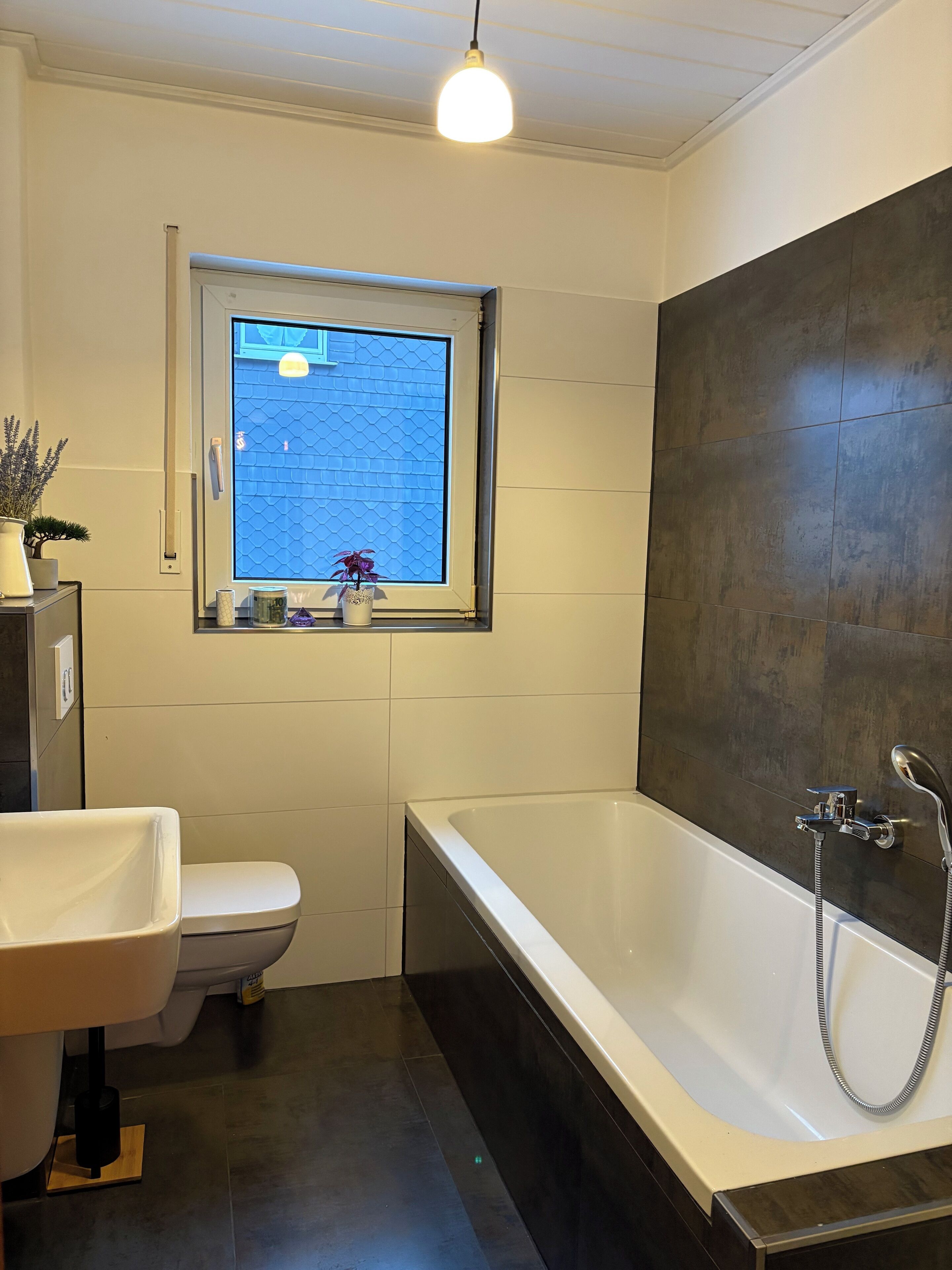 A modern bathroom with a bathtub, toilet, and a window with a view of a blue building.
