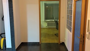 Ein Flur mit dunklem Holzboden, einer weißen Wand und einer Tür mit blauem Einsatz. Eine Leuchte hängt von der Decke.