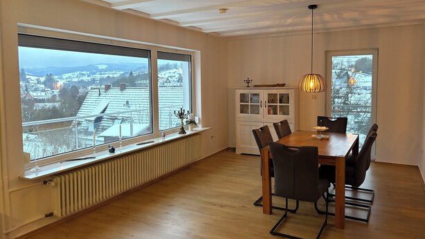 Ein Essbereich mit großem Fenster, einem Heizkörper, einer Vitrine und einer Pendelleuchte.