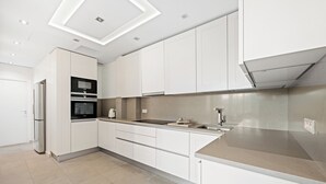 Una cocina moderna con armarios blancos, horno empotrado y refrigerador de acero inoxidable.