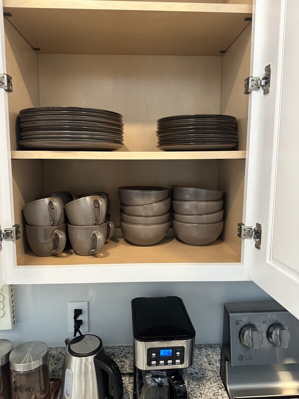 A kitchen cabinet with stacked plates and bowls, a coffee maker, and a kettle. - Home with fenced backyard in PCB 5 minutes drive to beach wide  parking lot (Panama City)