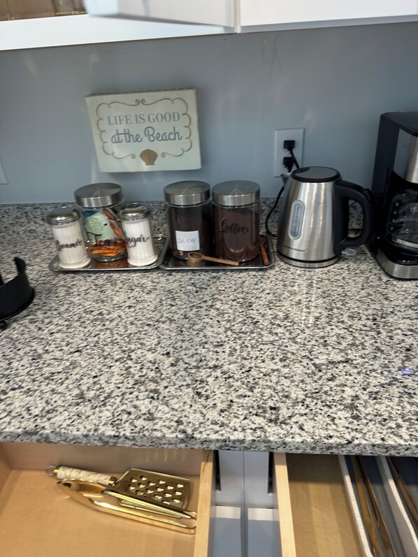 Una encimera de cocina con recipientes de acero inoxidable etiquetados con especias, una cafetera y un letrero que dice 'La vida es buena en la playa'.