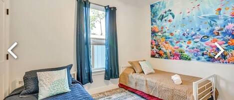 A bedroom with two beds, a ceiling fan, a window with curtains, and a mural of marine life on the wall.
