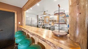 Een keuken met houten balken, een houten bar en groene krukken.