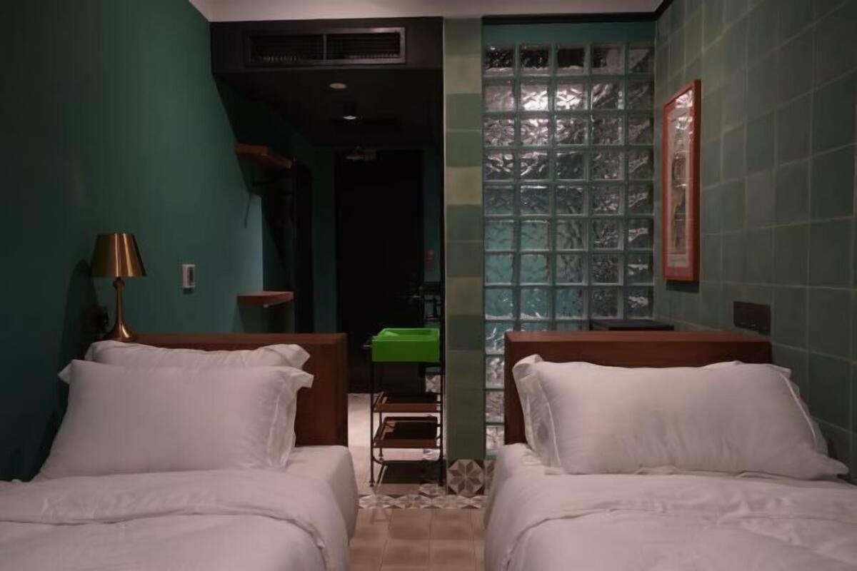 Een hotelkamer met twee bedden, een groene wand, een raam met uitzicht en een groene wastafel.