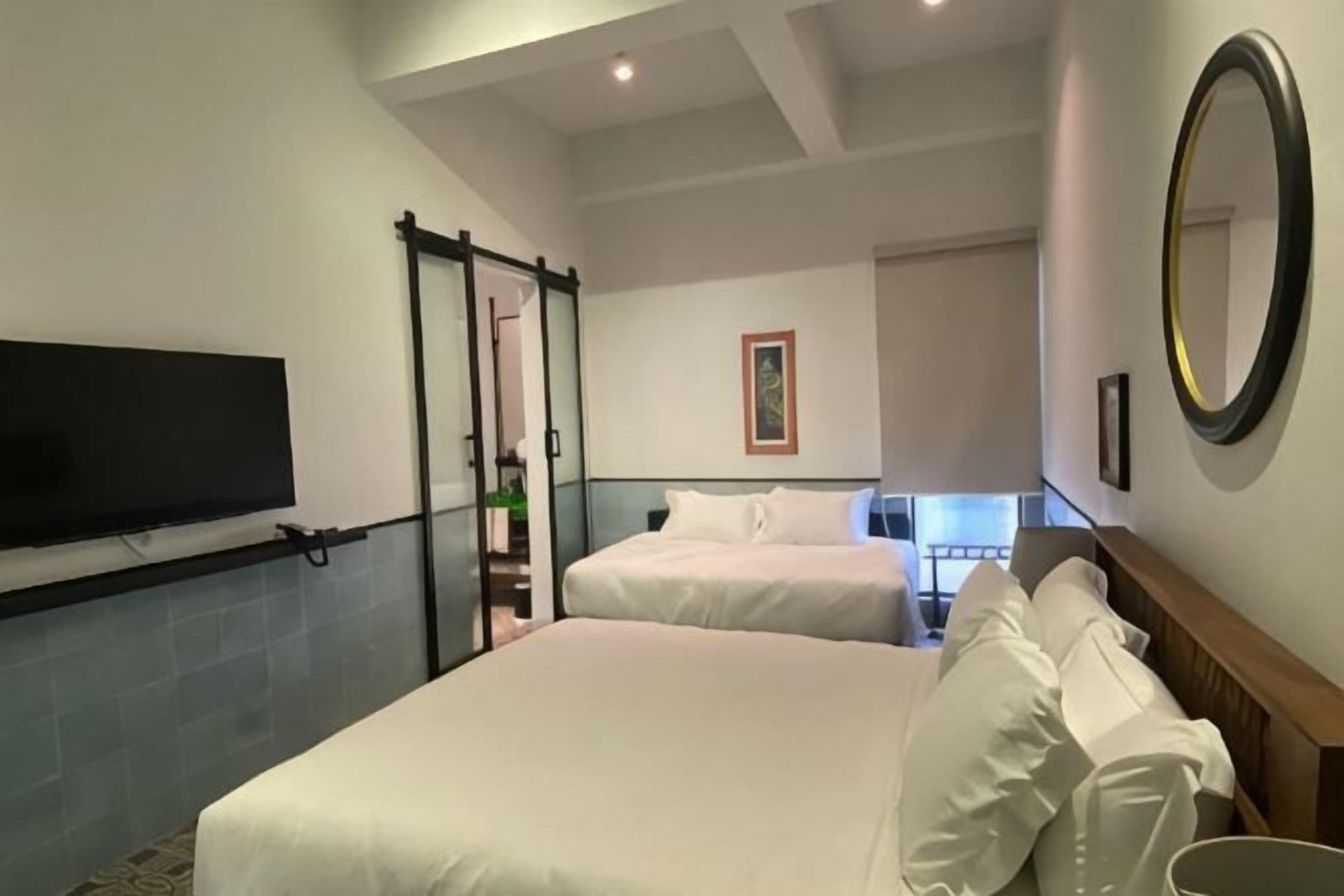 Habitación de hotel con dos camas, televisor, un espejo grande y vistas a un balcón.