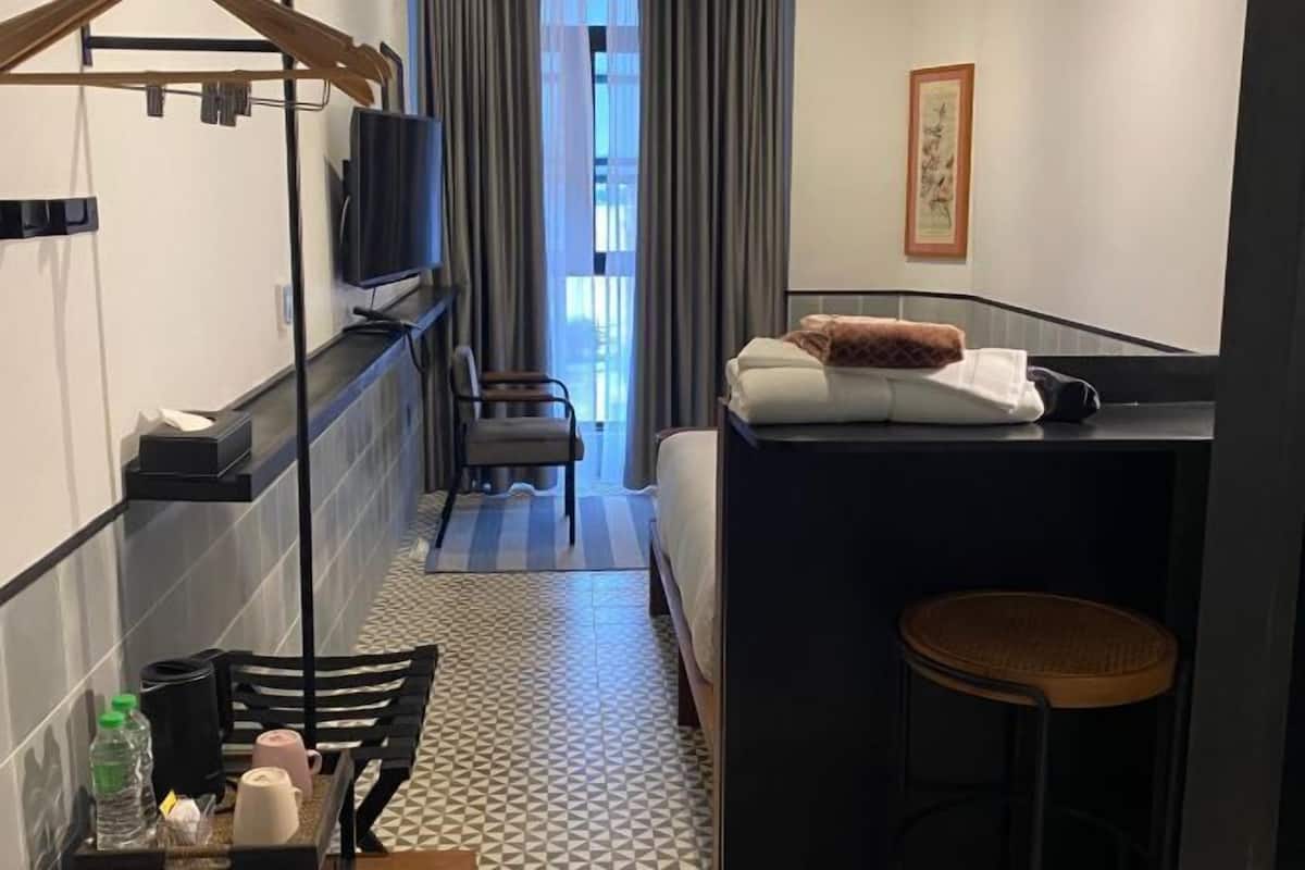 Een hotelkamer met een bed, een televisie, een bureau met stoel, een kleine tafel met stoel, en een raam met gordijnen.