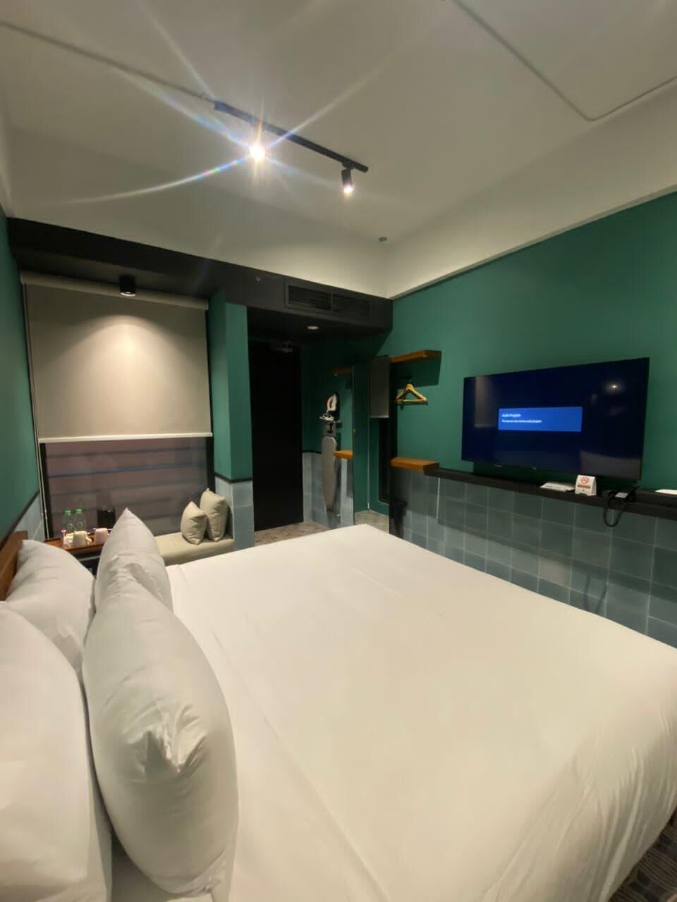 A modern hotel room with a large bed, a flat-screen TV mounted on the wall, and a bathroom with a mirror and towel rack.