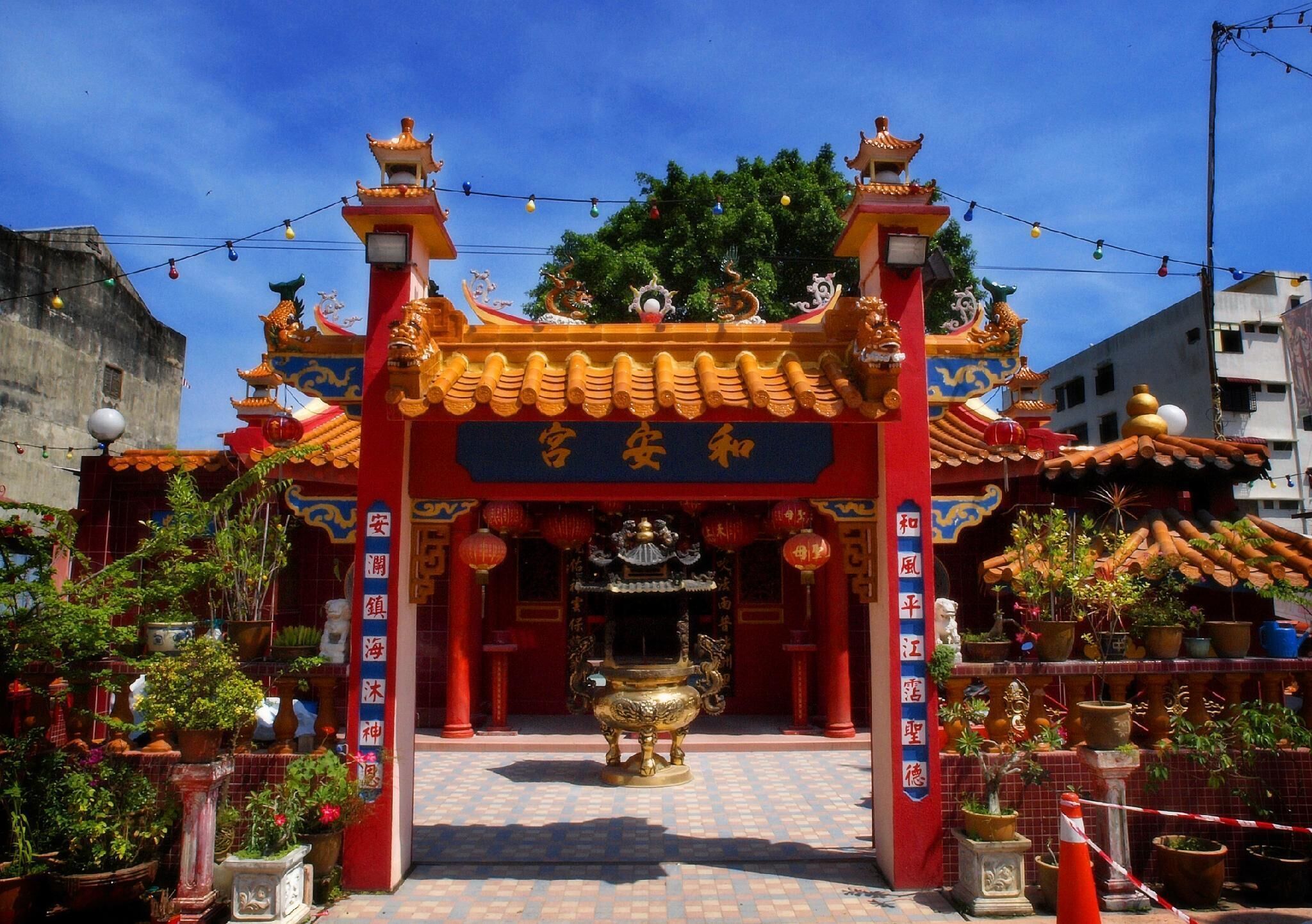 A traditional Chinese temple with ornate architecture, a central altar, and surrounding potted plants.