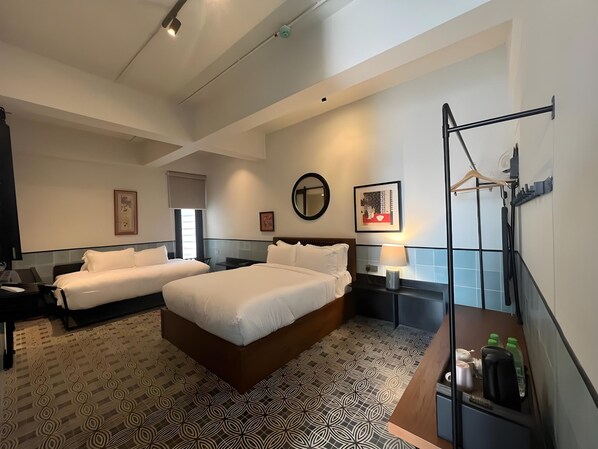 Habitación de hotel con dos camas, un escritorio, una silla, un espejo y un perchero.