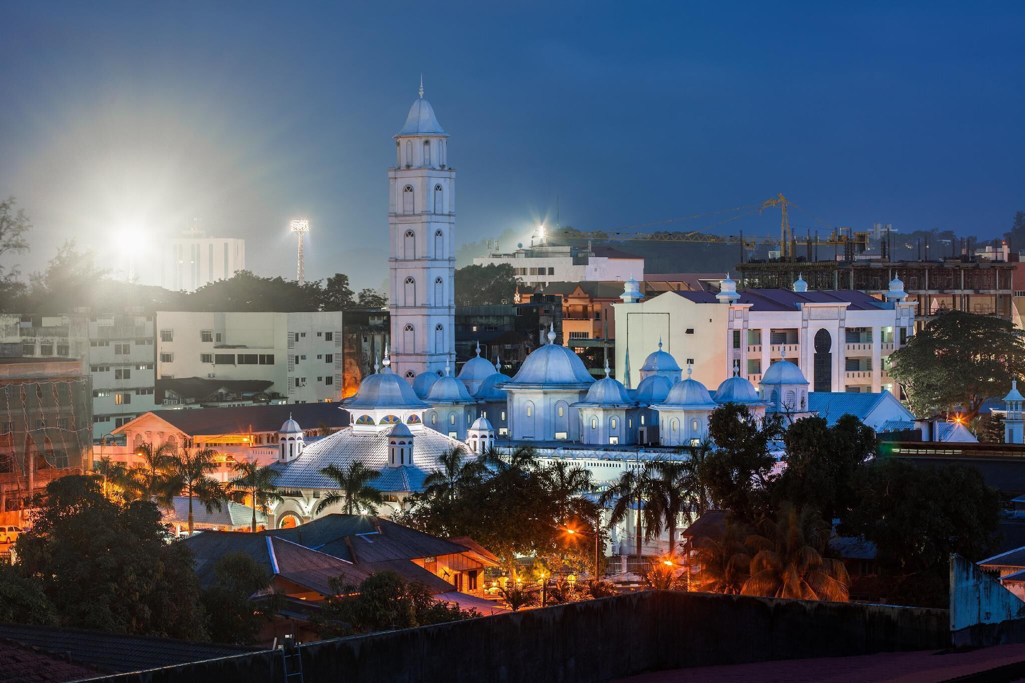 A historic building with a prominent bell tower and multiple domed structures, surrounded by modern buildings and palm trees.